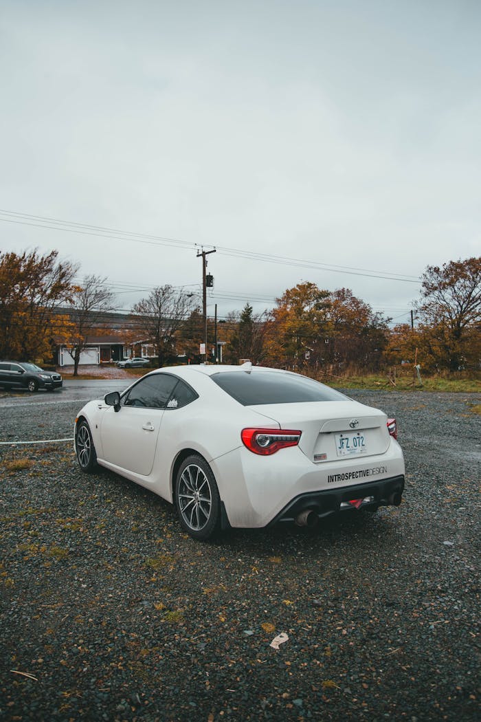 White Toyota parked on a gravel lot with autumn foliage in the background.
